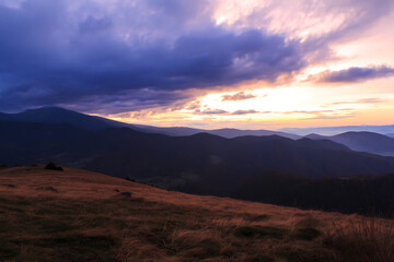 Dramatic Sunset Over Rolling Mountain Ranges with Golden Grasslands.
