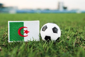 Algeria flag and soccer ball on green grass field. International football tournament concept with stadium background. Perfect for North African sports editorial and news content. © The Dell Shot by SJ