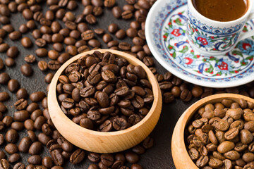 Fototapeta premium Two types of coffee beans are arranged in bamboo bowls with a cup of coffee on a black surface.