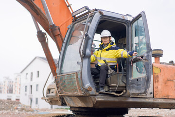Construction site excavator operator wearing safety helmet and reflective jacket operating heavy machinery
