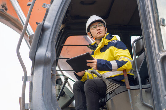 Engineer in excavator cab holding tablet while performing on-site work