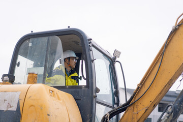 Construction worker wearing a safety helmet operates an excavator on-site during daytime work © zhu difeng