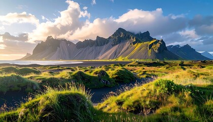 Scenic landscape view of black beach with grassy dunes and impressive mountain range against partly cloudy sky