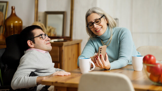 Woman and man with a physical disability using a smartphone and drinking coffee, sharing happy moments at home