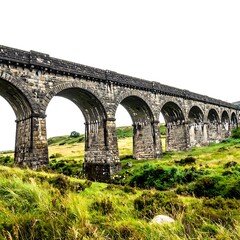 Stone aqueduct spans a grassy valley under an overcast sky. Arches fade into distant, hazy landscape
