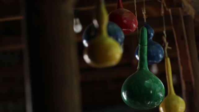 Close up shot of brightly colored hand painted bottle gourds hanging from a wooden ceiling. The colorful decorative gourds are strung up with twine in a rustic setting.