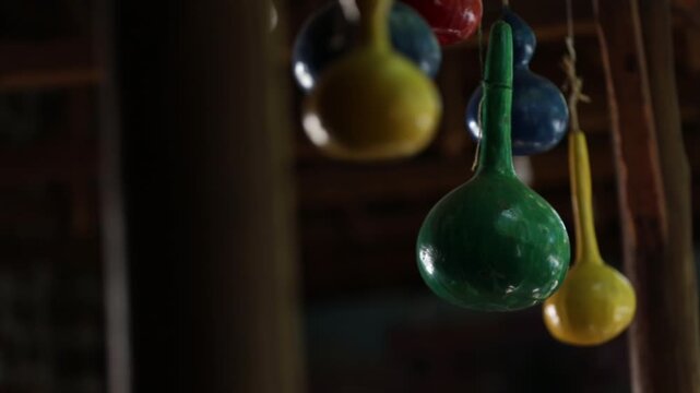 Close up shot of brightly colored hand painted bottle gourds hanging from a wooden ceiling. The colorful decorative gourds are strung up with twine in a rustic setting.