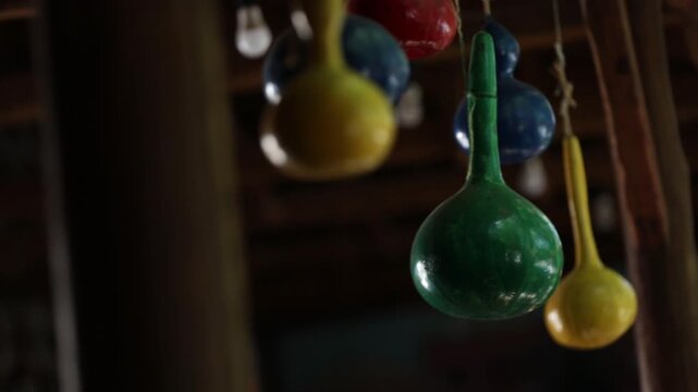 Close up shot of brightly colored hand painted bottle gourds hanging from a wooden ceiling. The colorful decorative gourds are strung up with twine in a rustic setting.