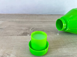 Laundry detergent spilling from green bottle into cap
