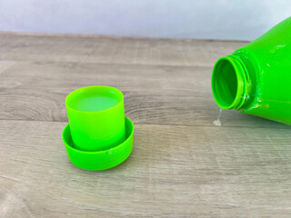 Green laundry detergent bottle spilling liquid on floor
