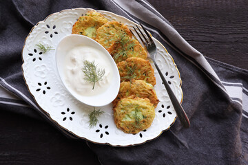 Healthy summer food, zucchini fritters. Vegetarian zucchini pancakes with cheese, served with sour cream on a rustic wooden table