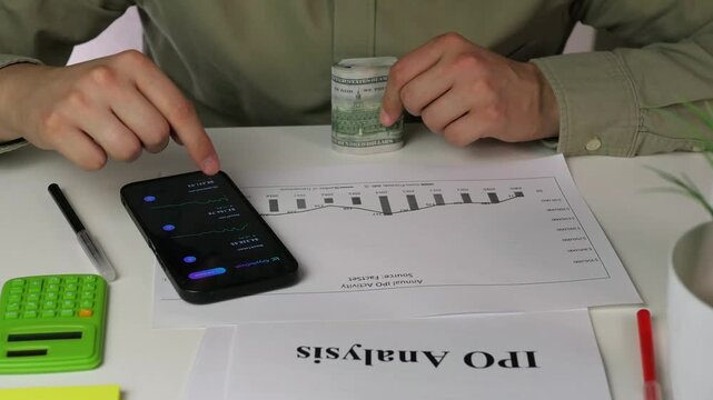 The analytical core of a high-stakes financial decision. This detailed close-up captures an investor in the midst of deep analysis, holding physical cash while cross-referencing IPO data on paper and
