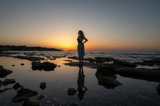Silhouette of woman with reflection in water mirror at sunset.
