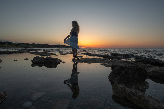 Silhouette of woman with reflection in water mirror at sunset.