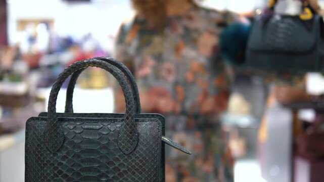 Luxurious genuine python snakeskin handbag on display in a store, with a female customer examining another purse in the blurred background, showcasing elegant and expensive fashion accessories