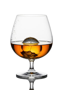 A flawless crystal snifter of aged single malt whiskey with a sphere ice cube on a reflective white background. Concept of premium spirits and luxury