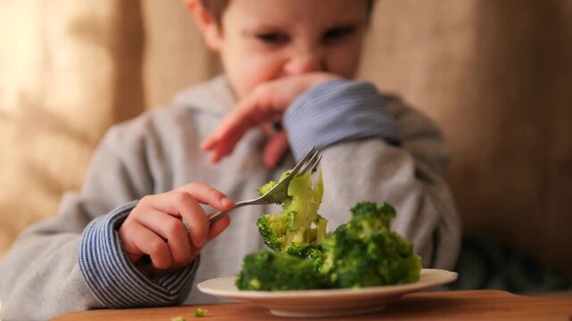 Child refusing to eat broccoli. A young boy expresses dislike and refuses a forkful of green vegetables, illustrating picky eating habits, childhood nutrition struggles, authentic family mealtime