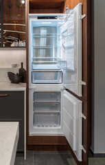Fototapeta premium Open empty built-in refrigerator with freezer in walnut kitchen cabinet