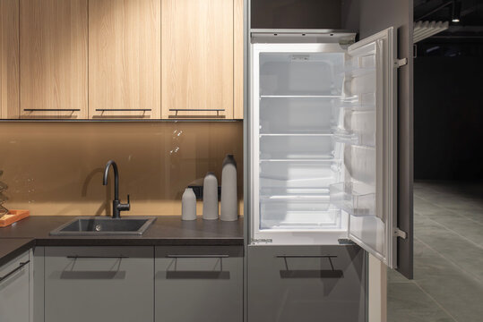 Open empty built-in refrigerator in modern gray and wooden kitchen