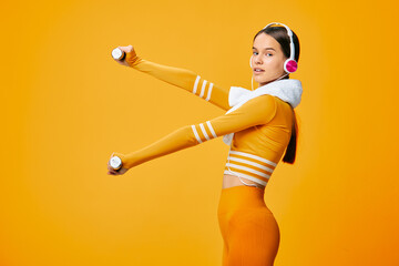 Naklejka premium Woman in bright orange sportwear lifts dumbbells with headphones against a vivid orange backdrop, showcasing fitness, exercise, movement and energetic sport-inspired training.