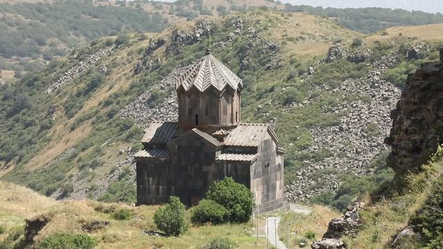 Picturesque view of an ancient Armenian church with a traditional dome, situated in a rugged mountain landscape. The historic stone building stands isolated amidst rocky hills and valleys.