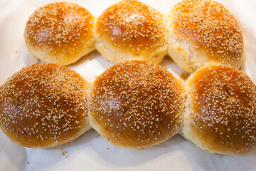 Freshly baked golden-brown sesame seed buns resting on white parchment paper near a kitchen stovetop