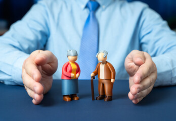 A man protects with his hands the figurines of a couple of elderly pensioners. Social protection...