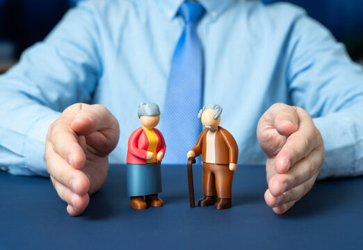 A man protects with his hands the figurines of a couple of elderly pensioners. Social protection and financial security. Support for seniors and pension insurance policy