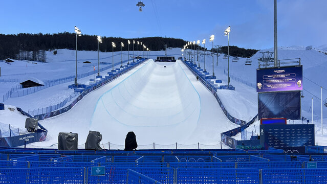 Livigno, Italy - February 20, 2026: Evening view of illuminated Milano Cortina 2026 Olympic halfpipe venue with blue fences, scoreboard and ski lifts in snowy Alps.