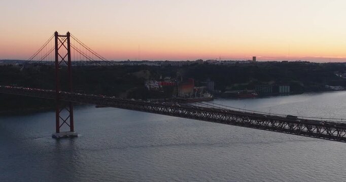 Establishing aerial drone shot of the red 25th April bridge in Lisbon, Portugal. Sunset dusk with traffic