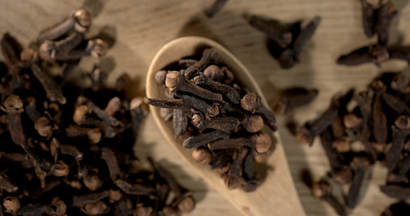 Whole cloves on wooden spoon with scattered cloves on table