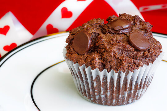 A decadent chocolate cupcake with chocolate chips set in a valentine's day backdrop.
