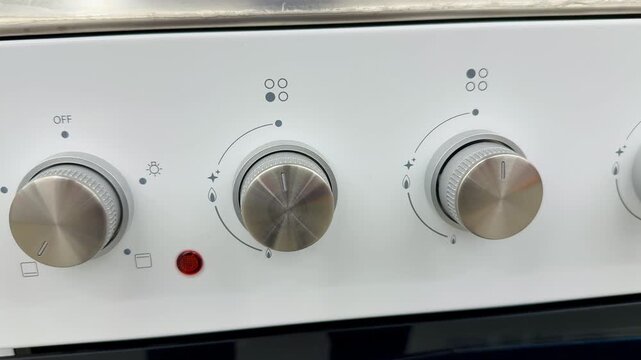 White electric stove with glass cooktop on showroom shelf, visible control knobs and mode dials, crisp enamel body, reflective.