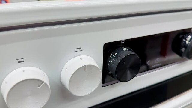 White electric stove with glass cooktop on showroom shelf, visible control knobs and mode dials, crisp enamel body, reflective.