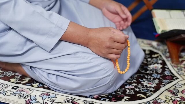Close-up of hands reciting dhikr using prayer beads against a blurred background. Hands reciting dhikr. A man reciting dhikr while holding a prayer beads. A Muslim's worship activity.
