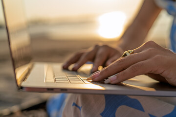 Person typing laptop keyboard by sunset light