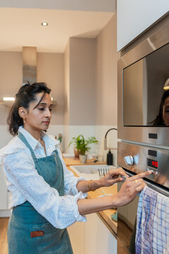 Woman Adjusting Oven Timer In Modern Kitchen
