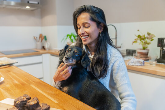 Woman Smiling While Petting Dog In Kitchen