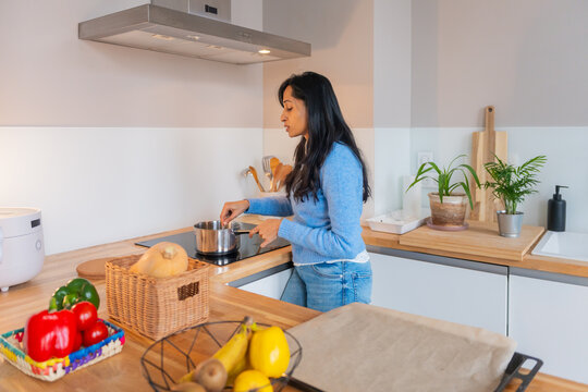 Woman Stirring Saucepan In Bright Kitchen