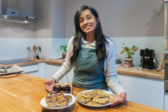 Portrait Of A Woman Displaying Cookies And Brownies In Kitchen