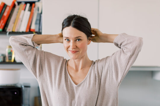 Smiling Woman Tying Hair in Kitchen