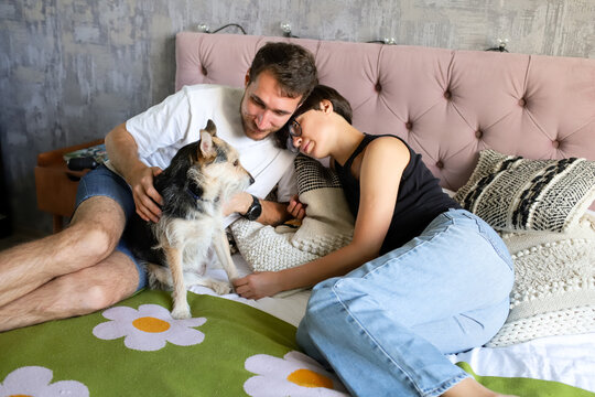 a woman and a man lie on a bed with a dog