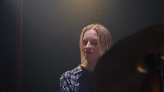 Beautiful drummer blonde girl performs solo on stage, sound checking before a rock concert. Woman bangs on a drum kit. Face of female musician bangs drumsticks in a snare drums, cymbals. Portrait