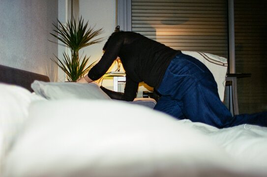 Anonymous woman in casual clothing adjusting bedding in cozy bedroom 