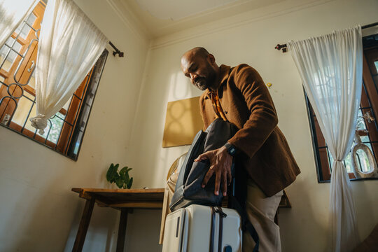 Man in Brown Jacket Securing Backpack on Suitcase