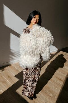 Stylish woman in fur coat standing in room