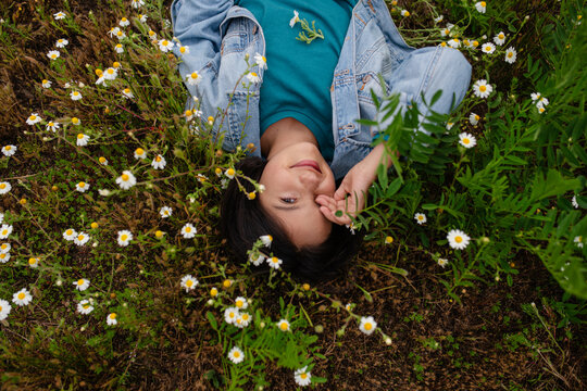 Little girl lying smiling on a grassy field with wild flowers.