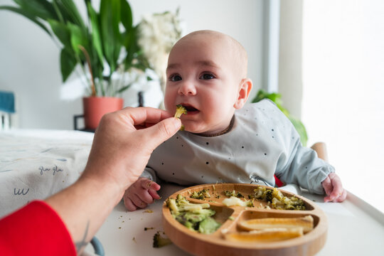 Mother feeding her baby with broccoli at home