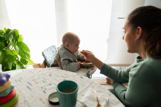 Mom feeding her baby solid food with a spoon at home