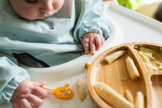 Baby eating solid food wearing bib in high chair